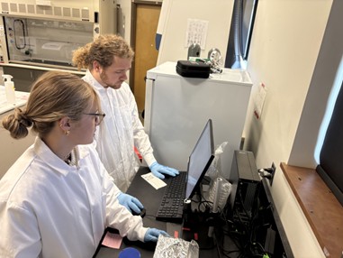 two people in white labcoats looking at a computer.
