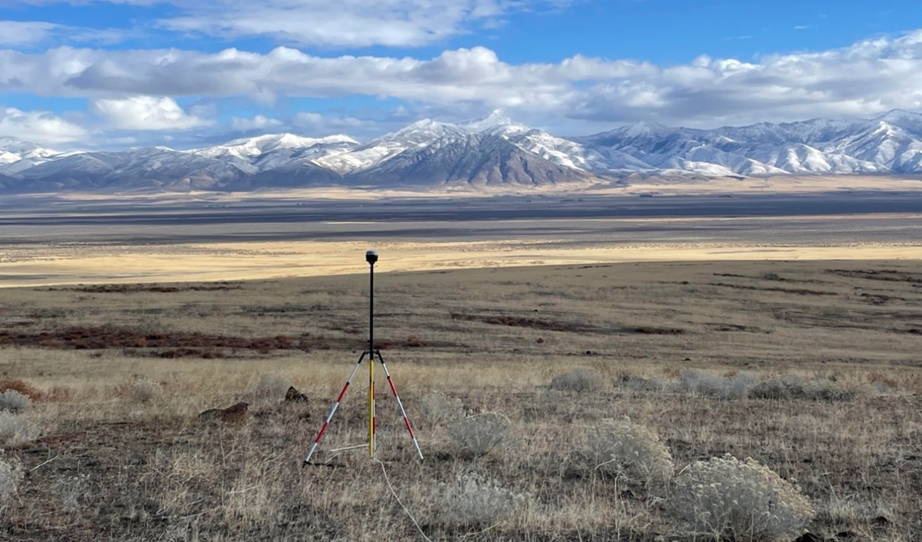 A sensor on a tripod in the Montana Plains with towering mountains in the background.